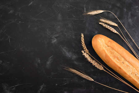Fresh french baguette and ears of wheat on a dark background. Top view with copy space. Bakery conceptの写真素材