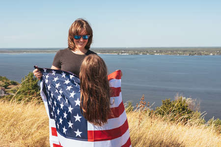 Happy family mom and daughter with american flag enjoy nature.