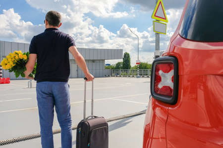 A man with a suitcase and flowers in an open car park. View from the back. Vacation conceptの写真素材