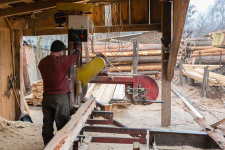 A worker works on sawmill equipment. Wood processing work process. timber industry.の写真素材