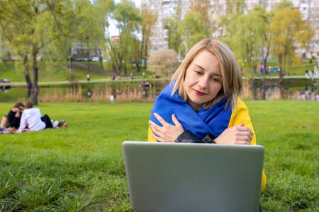 Outdoor portrait of a Ukrainian girl talking online using a video call on a laptop in the park.の写真素材