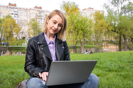 Beautiful young woman sitting in the park with a laptop. Urban lifestyle.の写真素材