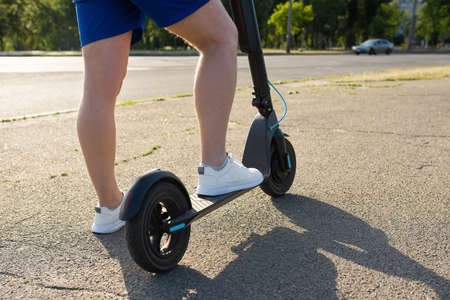 Legs of a man on an electric scooter on the road in summer. Urban transport concept