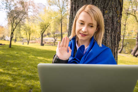 Happy young Ukrainian woman talking video call on laptop in park. The concept of remote communicationの写真素材