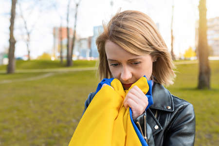 Outdoor portrait of sad woman holding Ukrainian flag in city park. Free lifestyleの写真素材