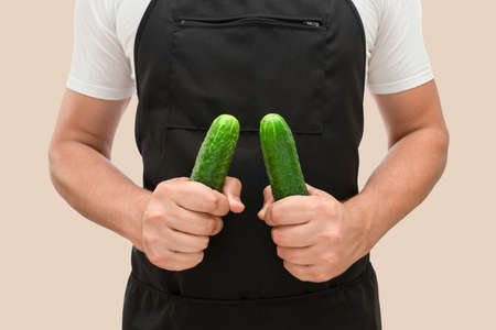 Fresh cucumbers in the hands of the cook isolated on a beige background. The concept of cookingの写真素材