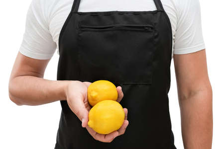 Torso of a man in a black apron with lemons in his hand on a white background. The concept of cookingの写真素材