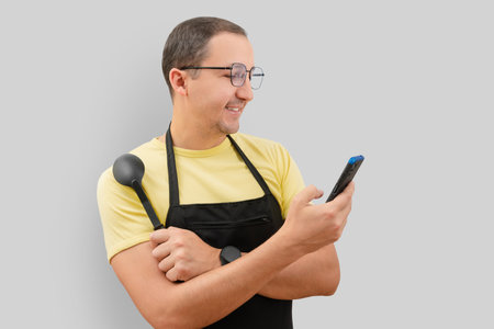 Portrait of a man in an apron and a phone in his hand on a gray background.の写真素材