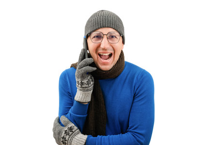 A young emotional man in warm clothes with a phone in his hands looks at the camera on a white background. Cold heating seasonの写真素材