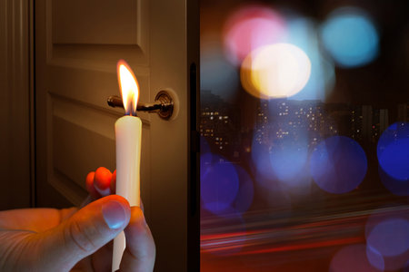 A burning candle in the hand of a man, against the background of the open door of the night cityの写真素材