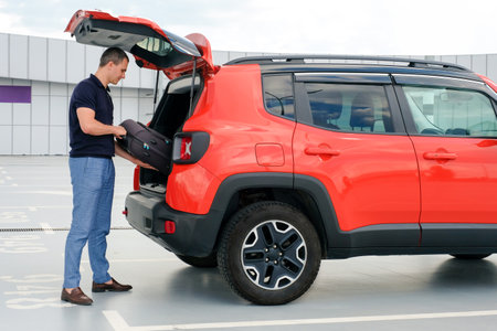 Young man puts a suitcase in the car in the parking lot. People lifestyles and transportation conceptの写真素材