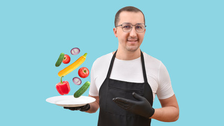 Cooking concept. Portrait of a man in a black apron with a plate of fresh food in his hands on a blue background. Healthy foodの写真素材