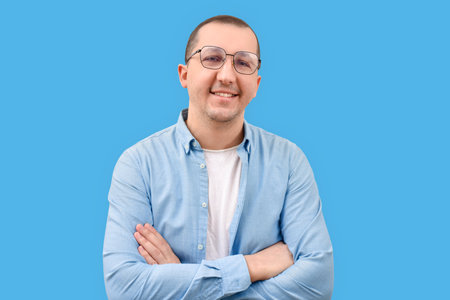Portrait of a confident young man in a denim shirt with crossed arms looking at the camera on a blue background.の写真素材
