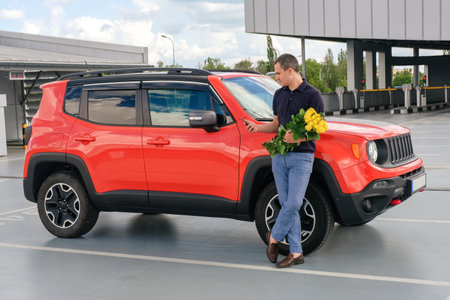 A man with a bouquet of flowers stands near the car in the parking lot of the airport.の写真素材