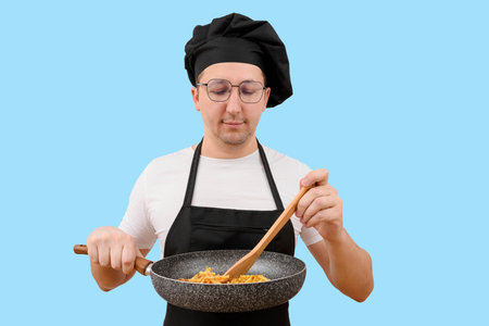 Male chef holding a frying pan prepares food on a blue background. Cooking and people conceptの写真素材