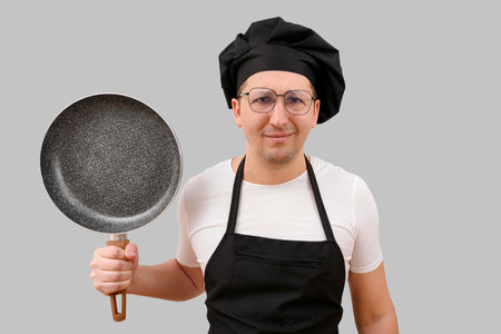 Chef with a frying pan in his hands on a gray background. Cooking and people conceptの写真素材