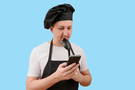 Young chef in a cap using a phone on a blue background. Cooking and people concept