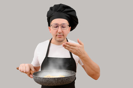 The cook prepares food in a frying pan on a gray background. The concept of the cooking processの写真素材