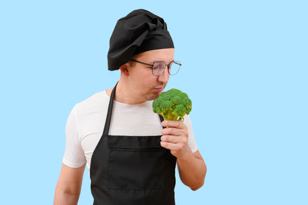 Man in apron and hat with broccoli vegetables on blue background. The concept of cookingの写真素材