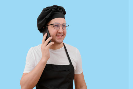 Young smiling chef talking on the phone on a blue background.の写真素材