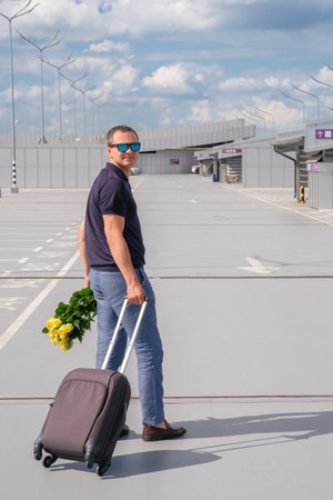 A man with a suitcase and flowers in an airport car park. Business trip. Vertical imageの写真素材