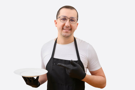Portrait of a man in an apron with a plate in his hand on a white background. The concept of cookingの写真素材