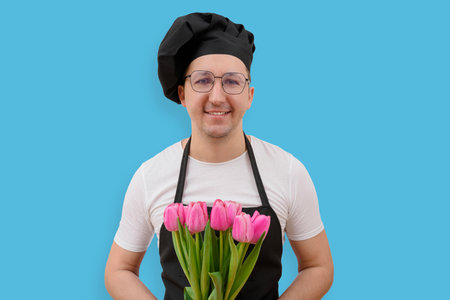 Happy cook holding flowers looking at camera on blue background. Cooking and people conceptの写真素材