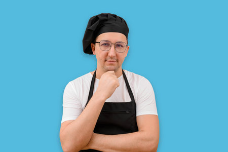 Portrait of a cook in an apron looking at the camera on a blue background. The concept of cookingの写真素材