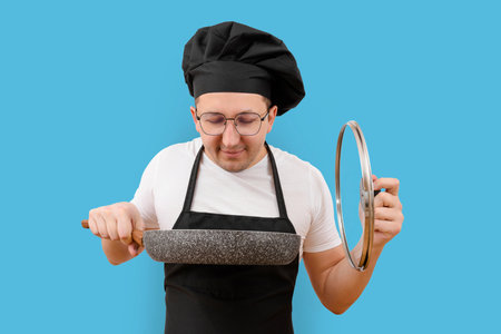 Young cook with a frying pan in his hand on a blue background. Cooking conceptの写真素材