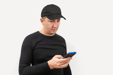 Young man in a baseball cap using a phone on a white background.の写真素材