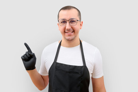 A man in an apron on a white background points his finger at an empty space for menu text.の写真素材