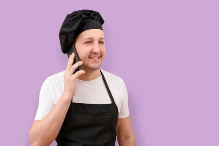 Smiling male chef using mobile phone on purple studio background. The concept of cookingの写真素材