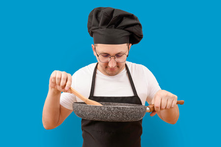Young cook with a frying pan in his hand on a blue background. Cooking and people conceptの写真素材