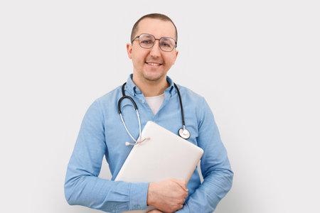 Young friendly male doctor with a laptop on a light background.