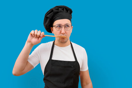 A male chef is tasting food from a spoon on a blue background.の写真素材