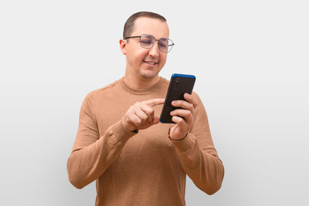 A young man in a sweater uses a phone on a gray background.の写真素材