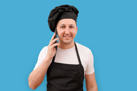 Male chef talking on the phone on a blue background. Cooking and people conceptの写真素材