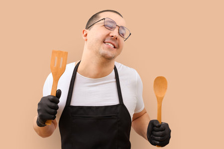 Happy chef in an apron with wooden spoons in his hands on a yellow background.の写真素材