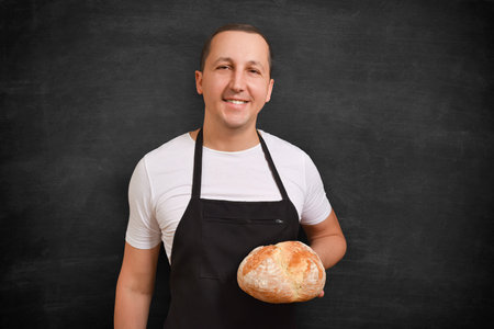 Happy chef with bread in hand looking at camera on dark background.の写真素材