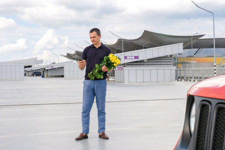 A man with flowers in his hands in the parking lot using the phone.の写真素材