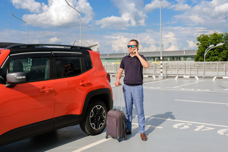 Young man with a suitcase in a parking lot using a phone.の写真素材