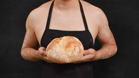 Chef in a black apron with bread in his hands on a black background.の写真素材