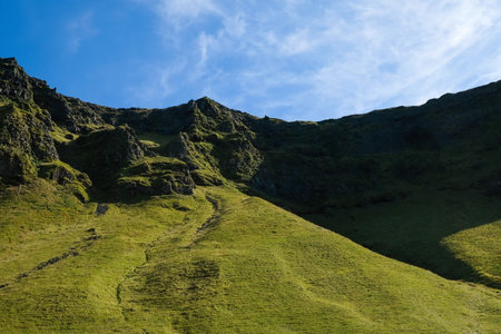 View of a mountain range covered with green grass against a cloudy sky on a sunny dayの写真素材