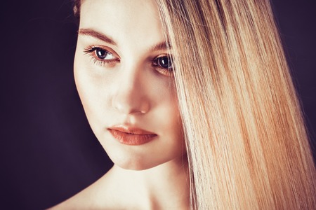 Beautiful young blonde woman with long straight hair on a dark backgroundの写真素材