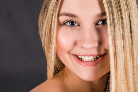 Beautiful young blonde woman with long straight hair on a dark backgroundの写真素材