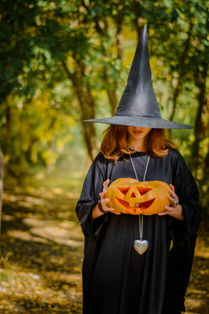 Happy halloween witch girl keeps orange pumpkinの写真素材