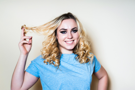 Blonde woman on a light background turns the lock of hair with your finger. Close-upの写真素材