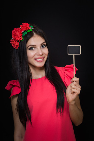 Beautiful woman with a wreath of red flowers holds a wooden plaque. Close-upの写真素材