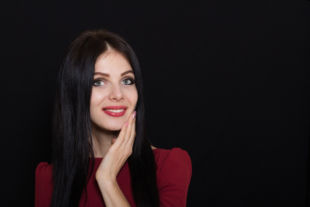 A beautiful woman with black straight hair and blue eyes in a burgundy dress on a dark background. Close-up. Space for textの写真素材