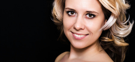 Close-up of a woman with blonde curls on a dark background smilingの写真素材